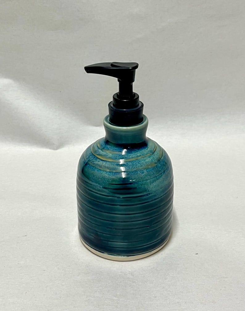 Pu&ograve; includere: Un dispenser di sapone in ceramica con una smaltatura lucida blu e verde acqua, caratterizzato da texture a coste orizzontali sul corpo. Il contenitore ha una forma arrotondata ed &egrave; dotato di una pompa in plastica nera funzionale.