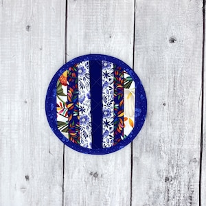 May include: A round blue and white quilted hot pad with a floral pattern. The hot pad is made of fabric and has a blue border.
