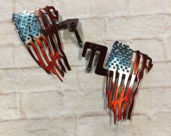 May include: Two metal American flag wall decor pieces with a distressed look. The flags are red, white, and blue with a faded, worn look. The flags are attached to metal brackets.