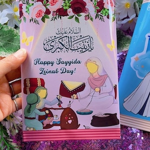 Puede incluir: Una tarjeta rosa y roja con un borde floral y una imagen de una mujer con un vestido blanco y un pañuelo en la cabeza. La tarjeta dice "Happy Sayyida Zeinab Day!" en inglés y árabe.