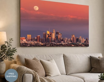 May include: A rectangular wall art canvas featuring a panoramic cityscape of Los Angeles at dusk. The sky transitions from a deep purple to a warm coral orange, illuminated by a full moon. The skyline displays numerous skyscrapers and buildings.