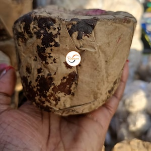 Könnte beinhalten: Nahaufnahme eines braunen, runden, verpackten Blocks aus Jaggery, einer Art unraffiniertem Rohrzucker, der in einer Hand gehalten wird. Der Jaggery ist in braunes Papier mit dunkelbraunen Flecken verpackt.