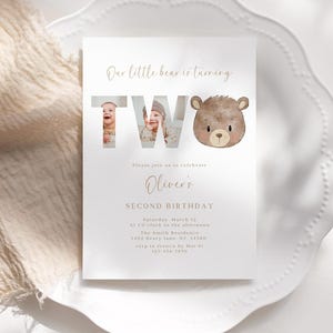 Puede incluir: Una tarjeta de invitación blanca con una ilustración de un oso marrón y el texto "Our little bear is turning TWO". La invitación es para una fiesta de segundo cumpleaños e incluye el nombre del niño, la fecha, la hora y la ubicación.
