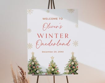 以下が含まれることがあります： 黒いイーゼルに立てられた白い看板。赤い筆記体で「WELCOME TO Oliver's WINTER Onederland」と書かれています。水彩画のクリスマスツリーと金の雪の結晶が描かれています。「December 20, 20XX」の日付も表示されています。