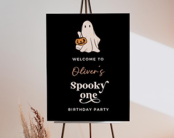 Könnte beinhalten: Schwarzes Schild auf einer Staffelei mit einem weißen Geist, der einen Kürbis hält. Auf dem Schild steht "WELCOME TO Oliver's Spooky One BIRTHDAY PARTY" in verschiedenen Schriftarten und Farben, ideal für einen Halloween-Geburtstag.