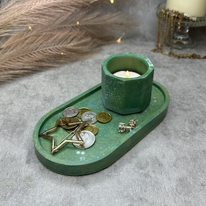 Pode incluir: Uma bandeja oval verde com um pequeno porta-velas verde e um enfeite em forma de estrela, moedas e brincos. A bandeja tem um acabamento salpicado.