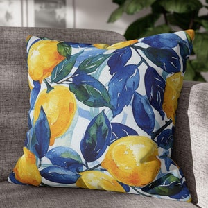 Puede incluir: Una almohada decorativa con un diseño de acuarela de limones y hojas azules sobre un fondo blanco.