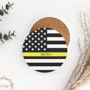 May include: A round coaster with a black and white American flag design. A thin yellow stripe is across the middle of the flag with the word "BROWN" printed in white letters.