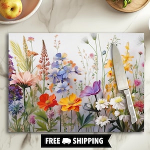 May include: A white glass cutting board with a colorful floral design featuring pink, blue, yellow, and orange flowers. The cutting board is on a white surface with a knife next to it.