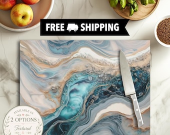 May include: A rectangular cutting board featuring a swirling abstract pattern of blue, teal, white, and gold tones. A stainless steel chef knife with a silver handle rests on the surface. The board displays a marbled design with metallic accents.