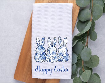 May include: White kitchen towel with three blue and white floral bunnies and the text "Happy Easter" printed on it.