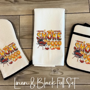 May include: A white oven mitt, towel, and pot holder set with black trim. Each item features the text "I only smoke good stuff" with a graphic of a grill. The set is made of linen.