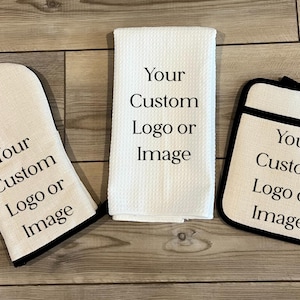 May include: A kitchen set featuring a white oven mitt, a white pot holder, and a white kitchen towel. Each item has a black border and the text "Your Custom Logo or Image". The items are on a wooden surface.
