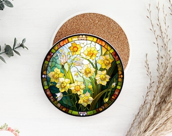 May include: A round ceramic coaster with a stained glass design featuring yellow daffodils on a green background. The coaster has a cork backing.