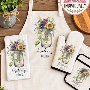 May include: A kitchen set featuring an off-white apron, a waffle-weave towel, an oven mitt, and a pot holder. Each item displays a mason jar filled with sunflowers and wildflowers, with the text Katie's KITCHEN printed below.