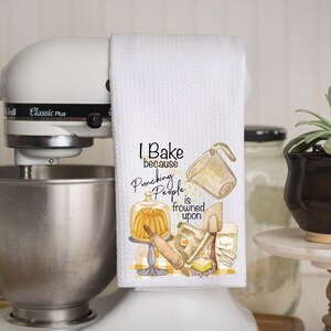 Pu&ograve; includere: Asciugamano da cucina bianco con un'illustrazione gialla e marrone di utensili da cucina e il testo "I Bake because Punching People is frowned upon".