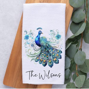 May include: White kitchen towel with a blue and green peacock design and the text "The Wilsons" printed on the bottom.