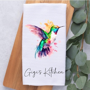 May include: White kitchen towel with a colorful hummingbird illustration and the text "Gigi's Kitchen" printed on it.