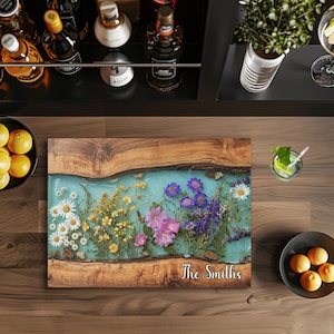 May include: A rectangular wooden serving board with a turquoise resin center, embedded with colorful flowers. The board is engraved with "The Smiths" in cursive. The board is surrounded by a wooden frame.