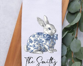 May include: White kitchen towel featuring a blue and white floral patterned bunny wearing a blue bow. The text "The Smiths" is printed below the bunny.