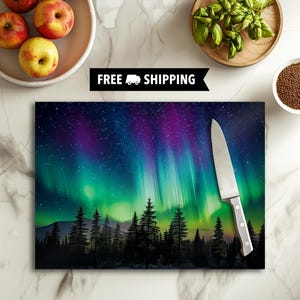 May include: A rectangular cutting board featuring a vibrant depiction of the aurora borealis with green and purple hues. A stainless steel knife rests on the board. The words "FREE SHIPPING" are displayed in a black banner.