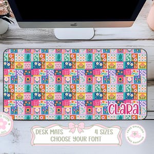 May include: A rectangular desk mat featuring a vibrant, multi-colored patchwork pattern of various floral and geometric designs. The name "CLARA" is printed in a bold, pink, rounded font in the bottom right corner of the mat.
