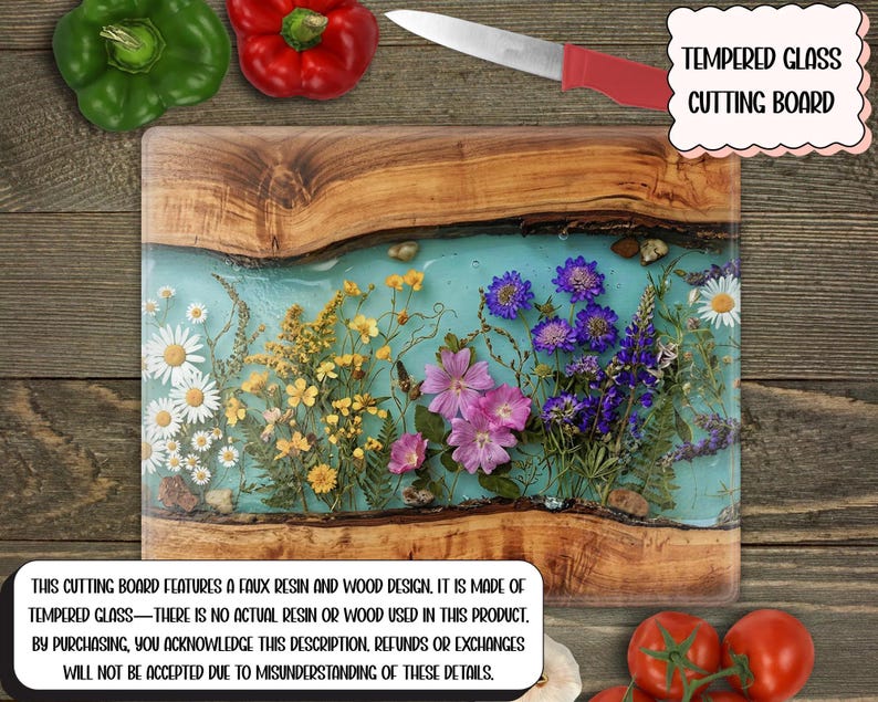 May include: Tempered glass cutting board with a faux resin and wood design. The board features a light blue resin center with embedded dried flowers. A knife with a red handle rests on the board. The text on the board reads: "TEMPERED GLASS CUTTING BOARD."