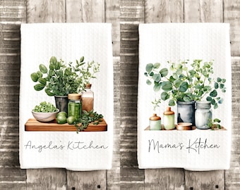 May include: Two white waffle-weave kitchen towels featuring watercolor illustrations of potted herbs, jars, and bowls on wooden boards. The left towel displays the text Angela's Kitchen, and the right towel displays the text Mama's Kitchen.