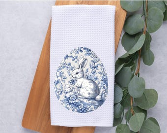 May include: White kitchen towel with a blue and white floral design featuring a rabbit and a baby rabbit inside an egg shape.
