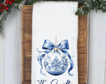 May include: White kitchen towel with a blue and white Christmas ornament with a blue bow and the text "The Smiths" printed on the bottom.