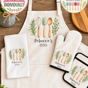 May include: A kitchen set featuring a beige apron, a white waffle-weave towel, an oven mitt, and a pot holder. Each item displays a watercolor illustration of a whisk, spatula, wooden spoon, and herbs with the text Rebecca's KITCHEN.