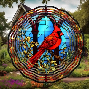 May include: A stained glass wind chime featuring a red cardinal perched on a branch with blue, green, and yellow leaves. The wind chime is surrounded by a circular metal frame with multiple layers.