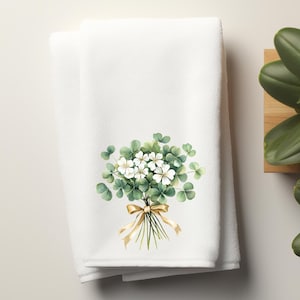 May include: White hand towel with a green shamrock and white flower bouquet with a gold ribbon.