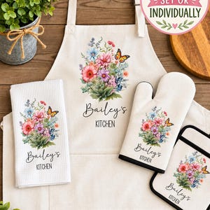 May include: A kitchen set featuring an apron, a waffle-weave towel, an oven mitt, and a pot holder, all in off-white fabric. Each item displays a colorful floral bouquet with a butterfly and the text Bailey's KITCHEN in black script and print.