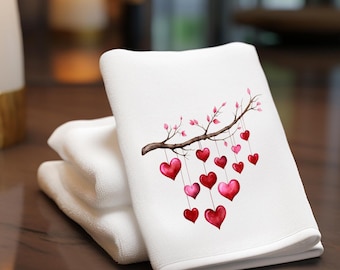 May include: White hand towels stacked on a dark surface. The top towel features a watercolor design of a brown branch with pink leaves and hanging red and pink hearts. The towels are soft and fluffy, perfect for bathroom decor.
