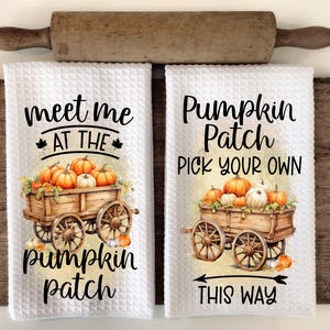 May include: Two white kitchen towels with a fall theme. One towel says "Meet me at the pumpkin patch" with a wagon full of pumpkins. The other towel says "Pumpkin Patch Pick Your Own This Way" with a wagon full of pumpkins and an arrow pointing to the right.
