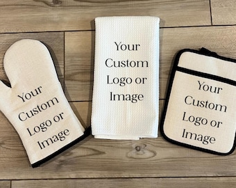 May include: A kitchen set consisting of an off-white oven mitt, a white waffle-weave kitchen towel, and a square pot holder, each featuring the black printed text Your Custom Logo or Image on the front surface of the fabric items.