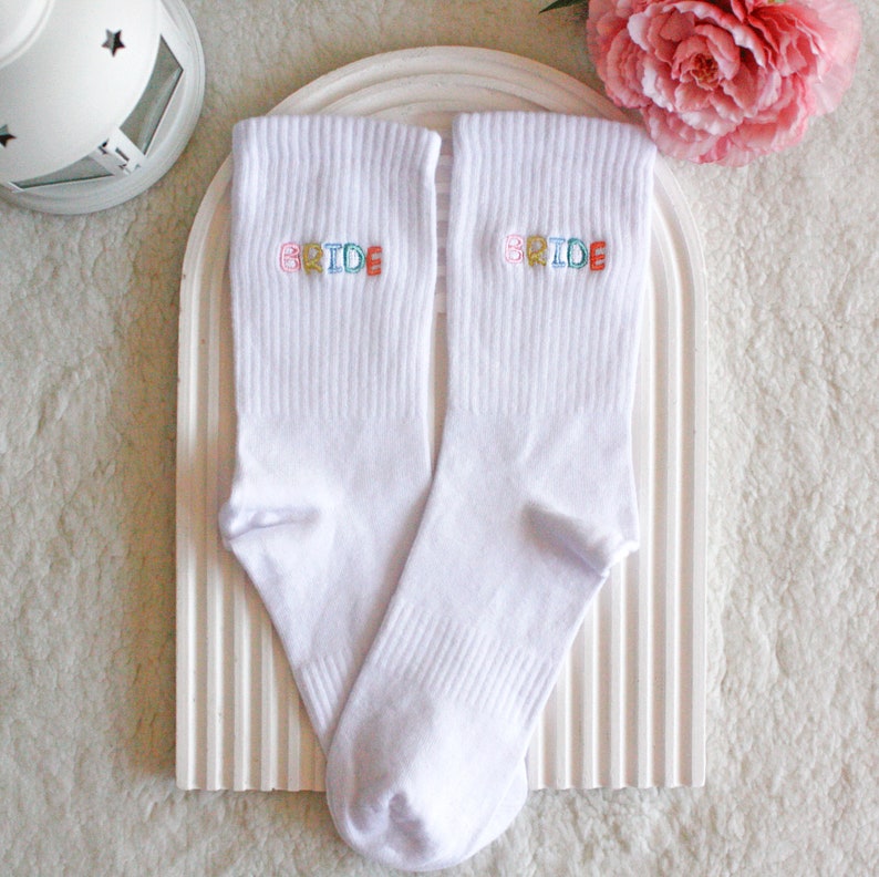 May include: A pair of white socks with the word "BRIDE" embroidered on each sock in colorful letters.