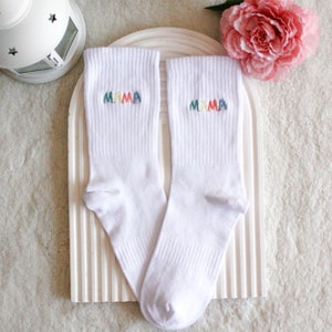 May include: A pair of white socks with the word "MAMA" embroidered on each sock in rainbow colors.