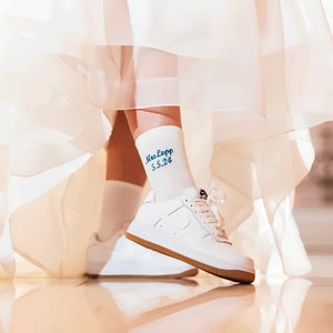 May include: White sneakers with blue embroidered text on white socks that reads "Mrs. Lepp 5.5.24". The sneakers are worn with a white tulle skirt.