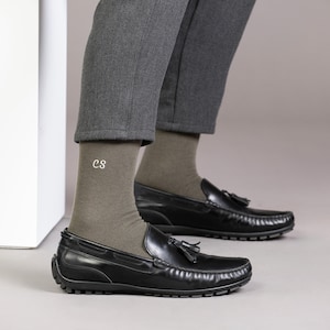 Puede incluir: Un par de calcetines verde oliva con las iniciales "CS" bordadas en un calcet&iacute;n. Los calcetines se llevan con mocasines de cuero negro con borlas.
