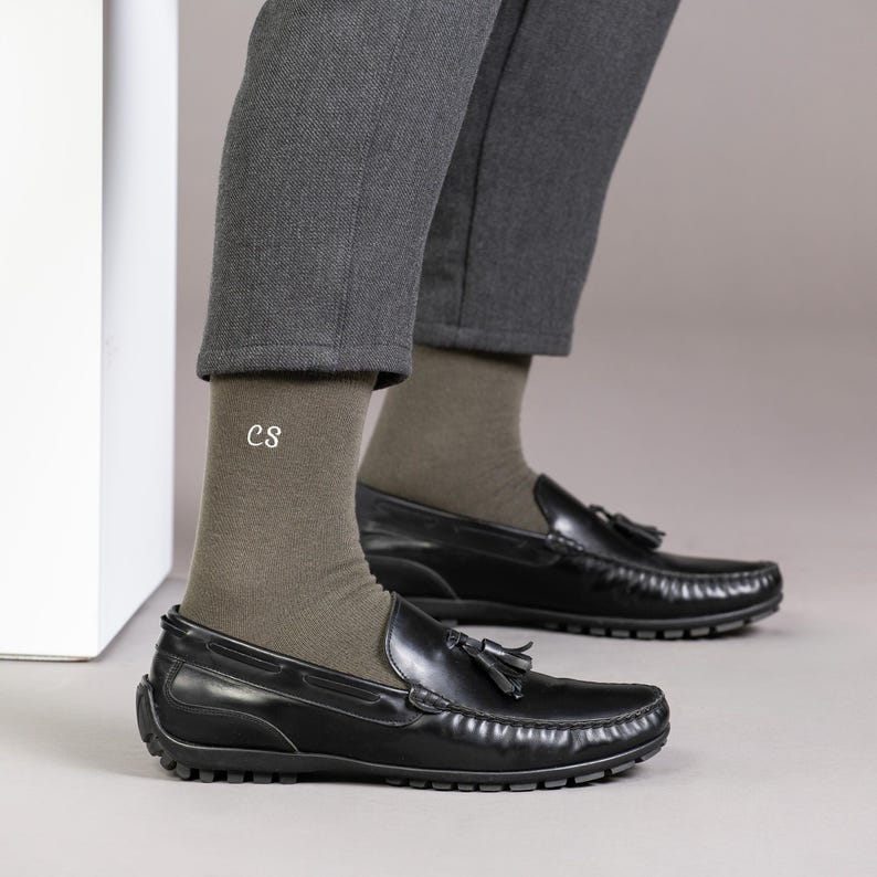 Puede incluir: Un par de calcetines verde oliva con las iniciales "CS" bordadas en un calcet&iacute;n. Los calcetines se llevan con mocasines de cuero negro con borlas.