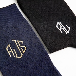 Puede incluir: Dos pares de calcetines con iniciales bordadas. Un par es azul marino con iniciales doradas "AJS" y el otro par es negro con iniciales blancas "RJ".