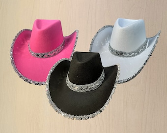 May include: Three cowboy hats with sequined trim. One hat is pink, one is white, and one is black.
