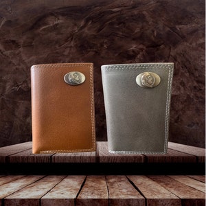 Puede incluir: Dos carteras de cuero, una marrón y otra gris, con un diseño en relieve plateado en la parte delantera. Las carteras están sobre una superficie de madera.