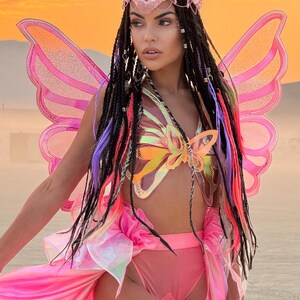 Puede incluir: Una mujer con un disfraz de mariposa rosa con alas iridiscentes, un top con forma de mariposa y una falda rosa. Lleva una diadema de cuentas con un dise&ntilde;o de mariposa.