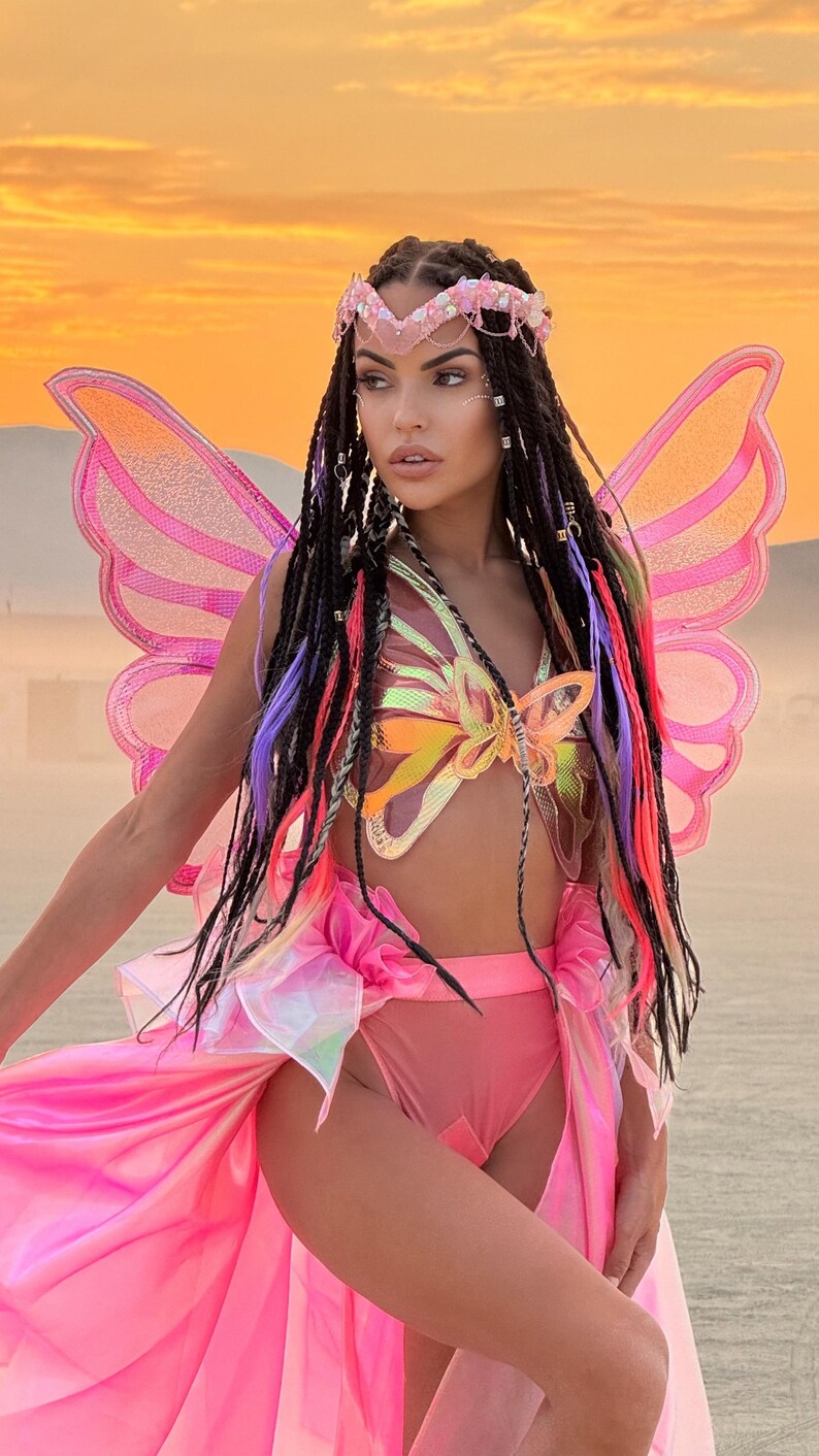 Puede incluir: Una mujer con un disfraz de mariposa rosa con alas iridiscentes, un top con forma de mariposa y una falda rosa. Lleva una diadema de cuentas con un dise&ntilde;o de mariposa.
