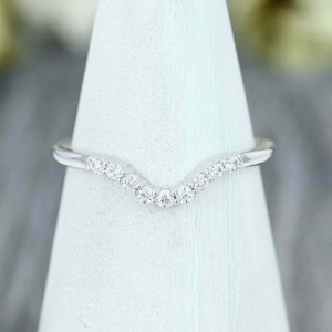 Puede incluir: Una fina banda de boda curvada con una fila de pequeños diamantes brillantes engastados en metal blanco.