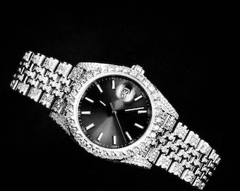 Pode incluir: Um relógio de pulso prateado com um mostrador preto e detalhes de diamantes na pulseira e no aro. O mostrador do relógio tem ponteiros e marcadores prateados, e uma janela de data na posição das 3 horas.