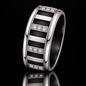 Peut inclure: Une bague large composée d'une monture en métal argenté poli avec une incrustation centrale noire mate. Le design présente une alternance de barres horizontales en métal argenté lisse et de barres argentées serties de trois petites pierres claires.